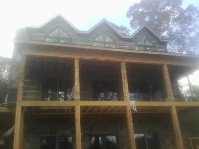 Dormers and porch framing on a large log home under construction — Roof Coating work by our crew in North
